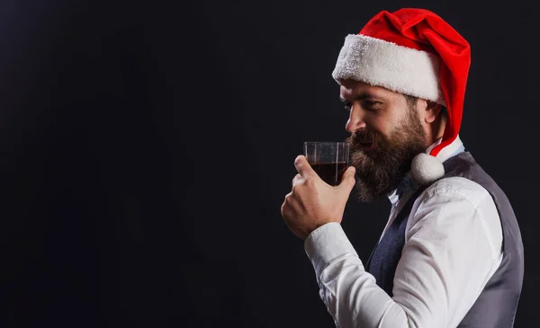 Brodaty facet w czapce Mikołaja ze szklanką whisky. Przyjęcie noworoczne. Degustacja whisky. Przestrzeń do reklam. — Zdjęcie stockowe