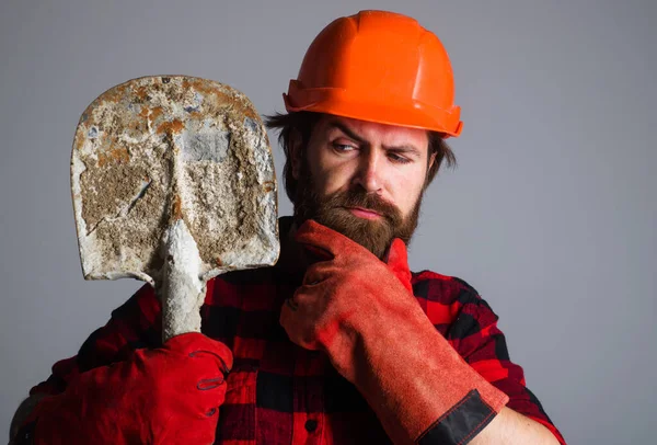 Építő kesztyűben és kemény kalap ásóval. Férfi munkás sisakban lapáttal. Szerelő vagy vállalkozó. — Stock Fotó
