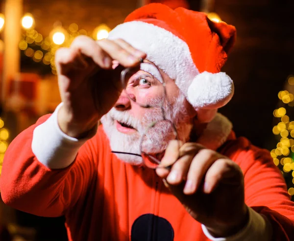 Mikołaj w potłuczonych okularach. Brodaty mężczyzna w stroju Mikołaja patrzący przez pęknięte okulary. Reklama świąteczna. — Zdjęcie stockowe