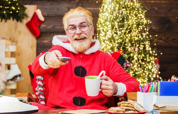 Санта Клаус сидит в кресле и смотрит рождественский фильм и пьет кофе. Концепция развлечений и кино. С Новым годом. — стоковое фото