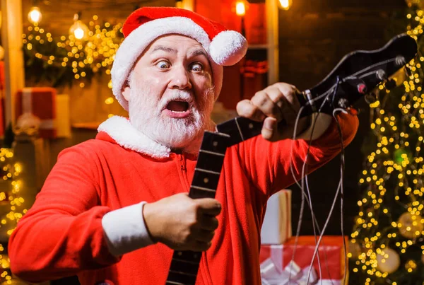 Zaskoczony Święty Mikołaj z zepsutą gitarą elektryczną. Wesołych Świąt i szczęśliwego Nowego Roku. Boże Narodzenie. Muzyka rockowa. — Zdjęcie stockowe