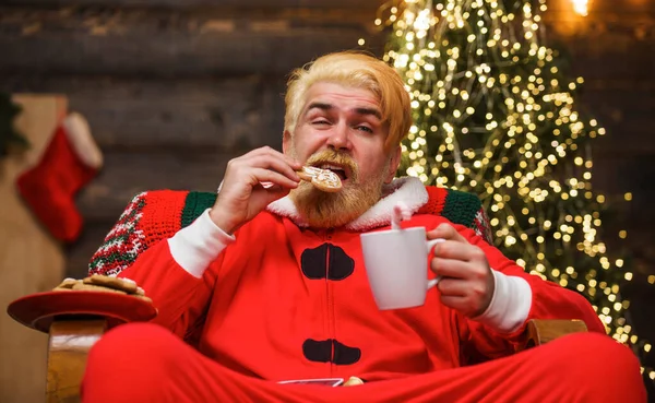 Santa Claus eat cookies and drinking milk. Bearded man in Santa costume relaxing at Home. Christmas. — Fotografia de Stock