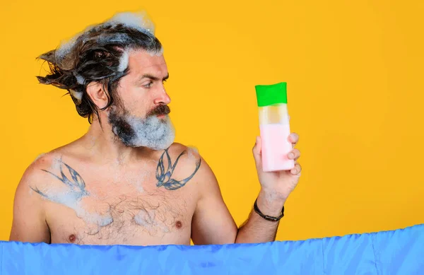 Man met shampoo fles. Man met baard die haar wast. Badtijd. Een man met schuim op zijn hoofd. Kopieerruimte. — Stockfoto
