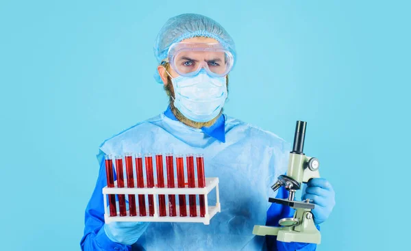 Médico en máscara médica con tubos de ensayo y microscopio. Científico analizando muestra de sangre en clínica. —  Fotos de Stock