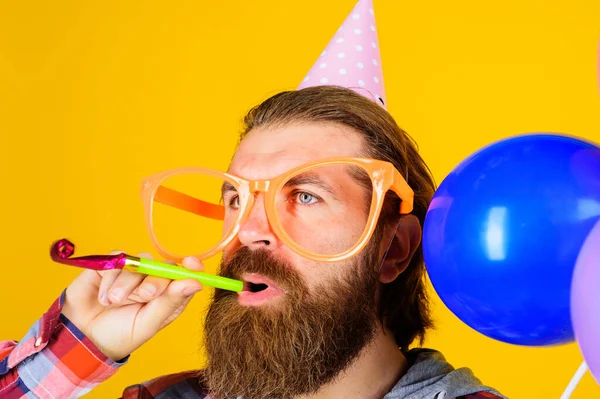 Hombre barbudo en gorra de cumpleaños con cuerno de fiesta. Varón en sombrero de cono de papel y vasos grandes con silenciador. — Foto de Stock