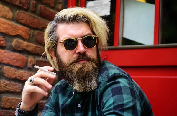 Szakállas férfi cigarettával. Egy közeli kép a füstölgő fickóról. Jóképű férfi dohányos napszemüvegben.. — Stock Fotó