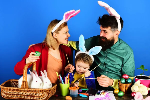 イースターの日。幸せな家族は卵を描く。ウサギの耳の中の母と父と息子. — ストック写真