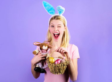 Paskalya Günü. Renkli yumurta sepeti ve peluş tavşan oyuncağıyla göz kırpan kız. Tavşan kulaklı mutlu kadın.