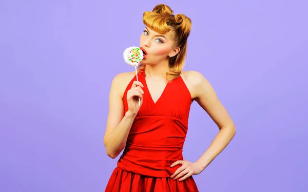 Szexi nő nyalókát nyalogat. Gyönyörű lány piros ruhában, cukorkával. Az érzéki nő szívja az édességet.. — Stock Fotó