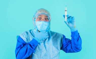 Koruyucu giysili doktor, gözlüklü ve şırıngalı tıbbi maske iğneye hazırlanıyor. Aşılama.