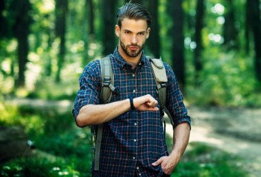 Sırt çantalı, kareli gömlekli yakışıklı sakallı adam ormanda saat yürüyüşüne bakıyor. Turizm, seyahat.