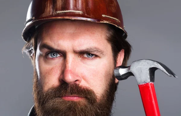 Szakállas férfi kalapáccsal. Szerszámok javítása. Építőmunkás, ács sisakban. Közelkép. — Stock Fotó
