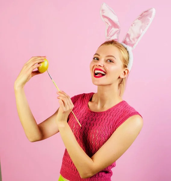 Пасхальная девушка в кроличьих ушах, рисует яйца. Женщина-кролик с цветным яйцом и кисточкой. — стоковое фото