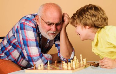 Grandfather teaching grandson to play chess. Senior man thinking about next move in game of chess.