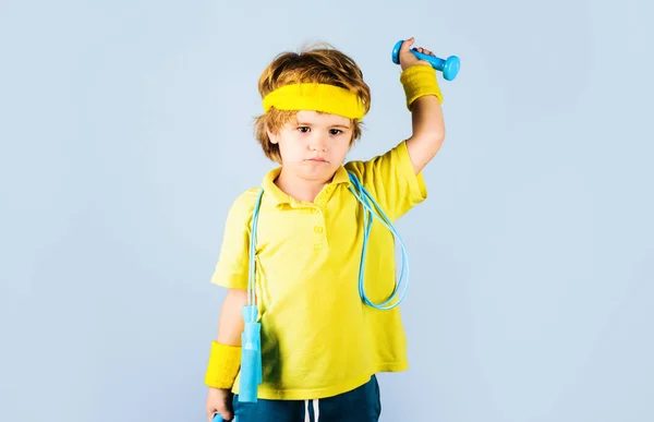 Sporty child with skipping rope and dumbbells. Kid boy sportsman with jump rope raised dumbbell. — Fotografia de Stock