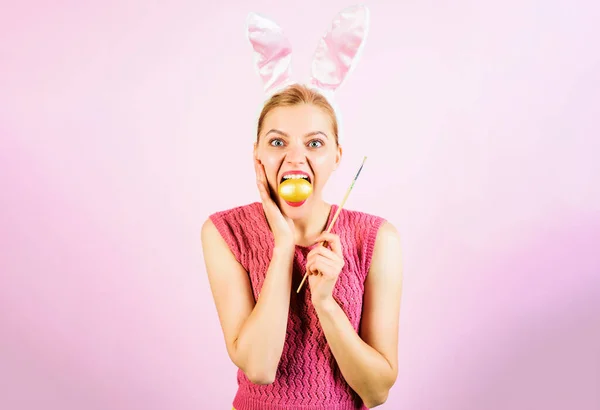 Easter rabbit girl in bunny ears with painting eggs. Surprised woman with color egg and paint brush. — Stockfoto