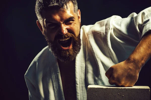 Karate hombre rompiendo con la mano de ladrillo de hormigón. Varón barbudo en kimono preparándose para la competencia. — Foto de Stock