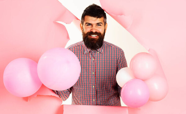Happy bearded man with pink balloons looking through paper hole. Party mood. Holiday celebration.
