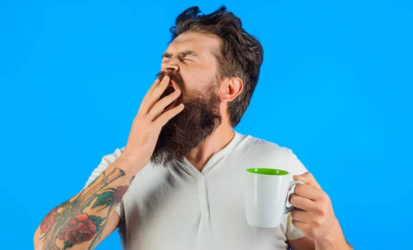 Homem barbudo sonolento a beber café. Um bocejo com caneca ou uma chávena de bebida quente. Refrigério matinal. — Fotografia de Stock