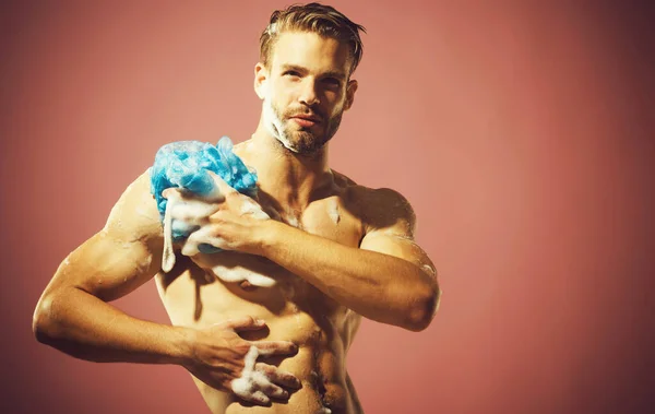 Handsome man washing in bathroom with shower gel and sponge. Sexy macho wash with soap foam. — Stockfoto