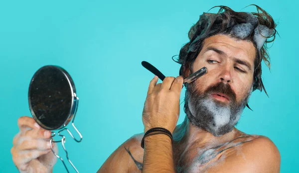 Een man met baard die zich scheert met een scheermes dat naar de spiegel kijkt. Dagelijkse ochtendroutine. Baard zorg. Kuuroord. — Stockfoto