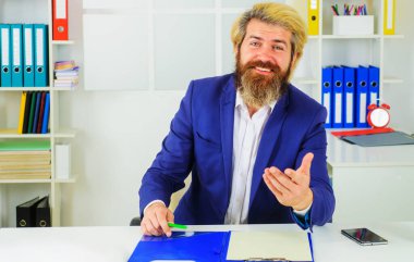 Takım elbiseli şık güler yüzlü iş adamı modern ofiste masa başında oturuyor. İş büyümesi. Liderlik. CEO..