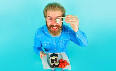 Sakallı adam yemek çubuklarıyla suşi yiyor. Bir tabak maki dürümü olan yakışıklı bir erkek. Japon yemeği.