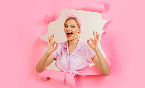 Улыбающаяся девушка показывает знак ОК, глядя через бумажную дыру. Женщина хорошо жестикулирует. Скидка. Продажа