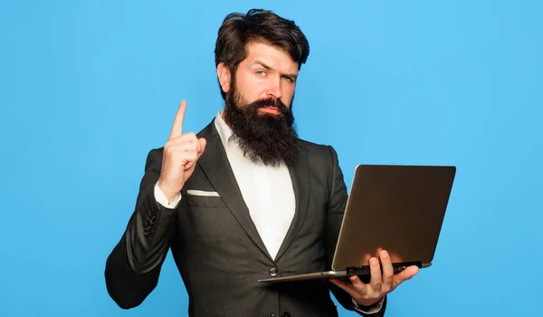 Bearded man with laptop computer pointing finger up. Businessman with notebook in office