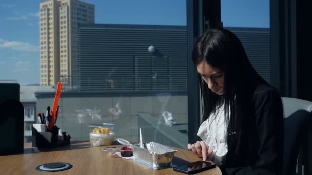 Empresária sentada no escritório ao almoço pela janela panorâmica, usa um telefone celular. Mulher de negócios na hora do almoço — Vídeo de Stock