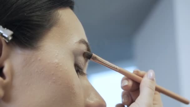 Τα μάτια ενός νεαρού γυναικείου μοντέλου κατά τη διάρκεια του μακιγιάζ. Ένας επαγγελματίας μακιγιέρ εφαρμόζει σκιές στο άνω βλέφαρο των μοντέλων ματιών με ένα απαλό πινέλο — Αρχείο Βίντεο