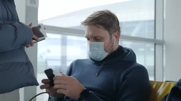 En man sätter på hörlurar och pratar med sin fru på flygplatsen under coronavirus pandemin i väntan på en försenad flygning — Stockvideo