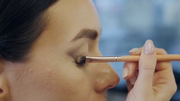 化粧中の若い女性モデルの目.プロのメイクアーティストは、柔らかいブラシでモデルの目の上まぶたに影を適用します。 — ストック動画