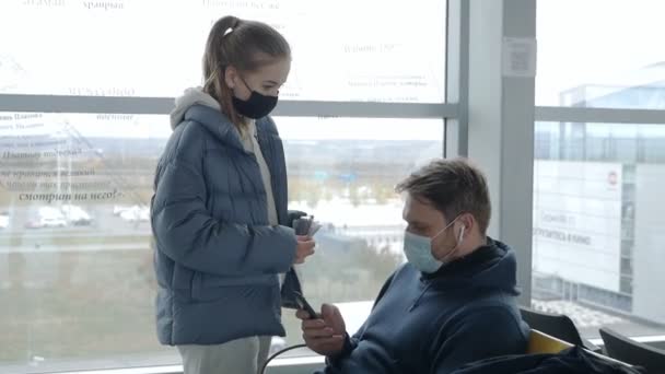 В аеропорту чекає пара з маскою. Чоловік і жінка в аеропорту під час пандемії коронавірусу в очікуванні затримки польоту — стокове відео