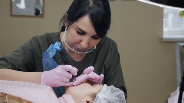 Le client du salon de beauté est allongé sur le canapé. L'esthéticienne applique un pigment permanent sur les lèvres. Procédure permanente de maquillage des lèvres. Industrie de beauté — Video