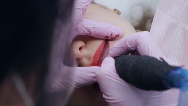 La main fait la procédure permanente de lèvres de maquillage appliquant le maquillage de pigment sur des lèvres avec la machine à tatouer — Video