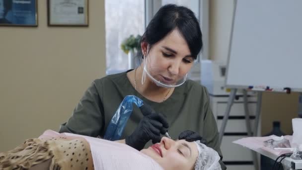 Cosmetologul aplică machiajul permanent pe sprâncene într-un salon de înfrumusețare. Procedura permanentă de machiaj într-un salon modern de înfrumusețare — Videoclip de stoc