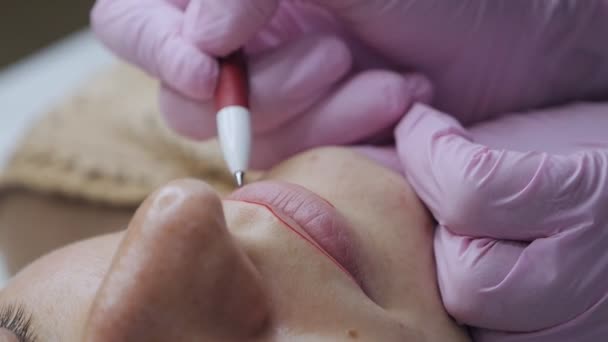 Concepto de labios rojos. Un procedimiento preparatorio antes de aplicar un tatuaje en los labios, el esteticista pinta los labios con una pluma, creando la forma y el contorno de los labios — Vídeos de Stock