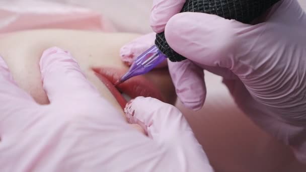 Cosmetologist appliquant le tatouage permanent de pigment rose sur les lèvres femelles avec la machine à tatouer d'aiguille au salon — Video