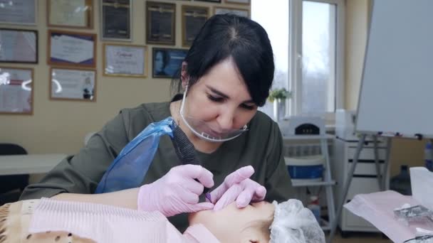 Kosmetikerin bei der Arbeit. Kosmetikerin mit Schutzmaske trägt im Salon eine dauerhafte Tätowierung mit Pigmenten auf Frauenlippen mit Tätowiernadel auf — Stockvideo