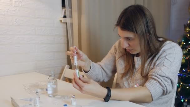 Jonge vrouw die een ampul met geneesmiddelen vasthoudt, de naald in de rubberen dop steekt en de spuit thuis vult — Stockvideo