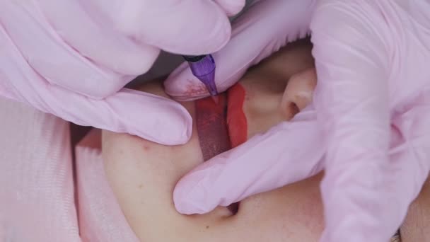 La main fait la procédure permanente de lèvres de maquillage appliquant le maquillage de pigment sur des lèvres avec la machine à tatouer — Video