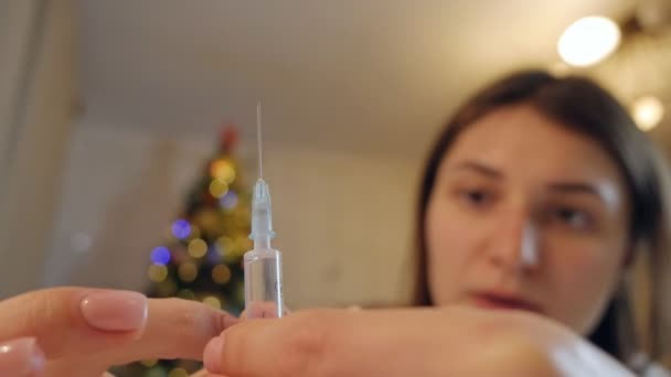 A young woman, at home, prepares a pre-filled syringe for injection by tapping on the syringe, ejecting a few drops from a hypodermic needle — Stock video