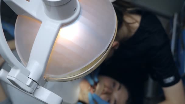 Uma mulher dentista trabalha com um paciente no consultório de dentistas, vista superior. Um paciente com um afastador de bochechas na boca em uma clínica odontológica moderna — Vídeo de Stock