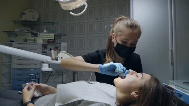 Uma jovem dentista mascarada e luvas médicas trabalha com um paciente em um consultório odontológico. Odontologia. Conceito de saúde e medicina — Vídeo de Stock