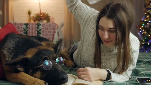 A beautiful girl lies on the sofa with her dog German Shepherd, against the backdrop of Christmas — Stock Video