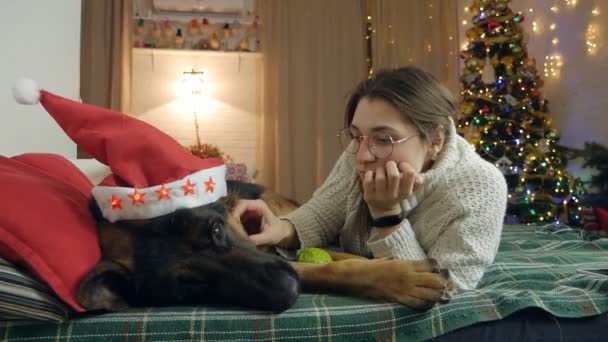 A beautiful girl lies on the sofa with her dog German Shepherd, against the backdrop of Christmas — Stock Video