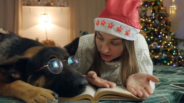 Mujer joven y perro en gafas están descansando en la cama en casa. Amor, unión y mascotas. mujer está leyendo un libro — Vídeo de stock