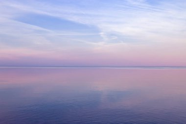 Denizde güzel bir gün batımı, suda pastel renkler ve yansımalar, renkli bulutlar ve deniz ile sakin doğa manzarası. Çevrenin doğal eğilimi. Soyut arkaplan.