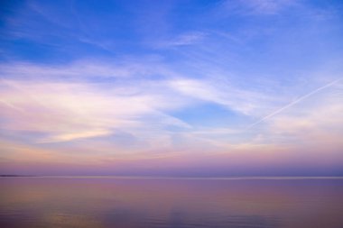 Günbatımında gökyüzü arkaplanı, renkli bulutlar. Deniz suyuna yansıyan doğa soyut kompozisyonu, ufuk çizgisinin doğal mavi mor tonları. Doğa ortamı.